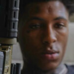 NBA Youngboy, the rapper, holding a gun in a contemplative pose.
