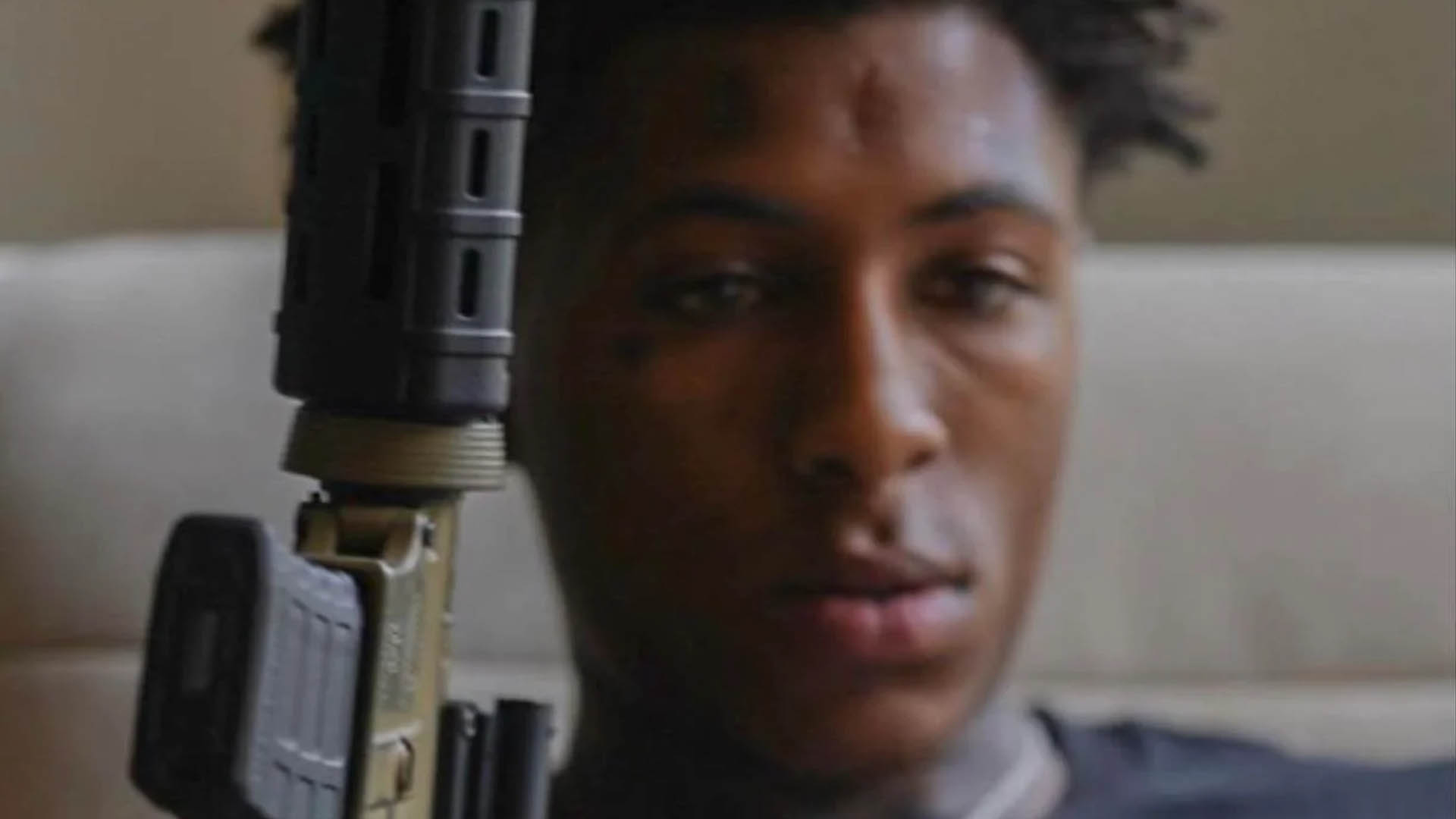 NBA Youngboy, the rapper, holding a gun in a contemplative pose.